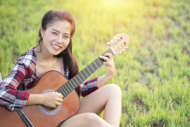 Çimlerde gitar çalan kadın güneş ışığıyla kapanıyor.