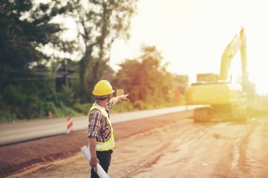 Makinelerle yol inşaatının planlarını elinde tutan mühendis.