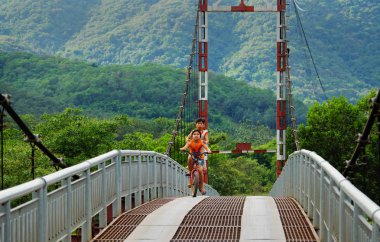 Vietnamese children ride bicycle on suspension bridge clipart