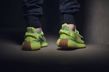Adidas Yeezy Boost 350 v2 Sply yarı donmuş sarı spor ayakkabılı koyu gri arka planda bir adam. Spor ayakkabılara yakından bak. Krasnoyarsk, Rusya - 26 Aralık 2017