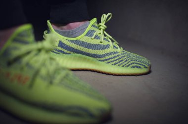 Adidas Yeezy Boost 350 v2 Sply yarı donmuş sarı spor ayakkabılı koyu gri arka planda bir adam. Spor ayakkabılara yakından bak. Krasnoyarsk, Rusya - 26 Aralık 2017