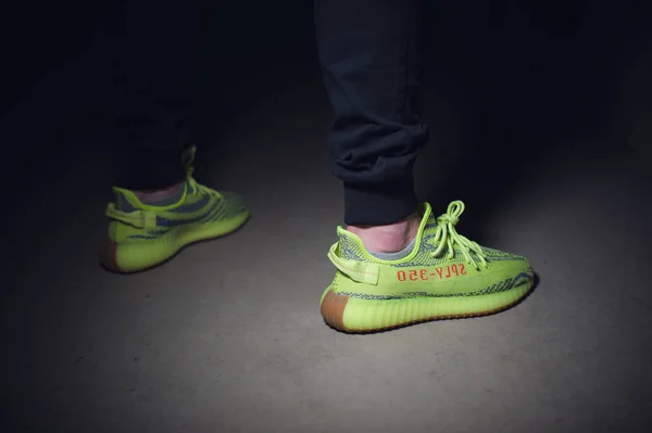 A man wearing Adidas Yeezy Boost 350 v2 Sply semi frozen yellow sport shoes shot on dark grey background. Close up view of sneakers. Krasnoyarsk, Russia - December 26, 2017 — 스톡 사진