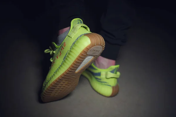 A man wearing Adidas Yeezy Boost 350 v2 Sply semi frozen yellow sport shoes shot on dark grey background. Close up view of sneakers. Krasnoyarsk, Russia - December 26, 2017 — Stock Photo, Image