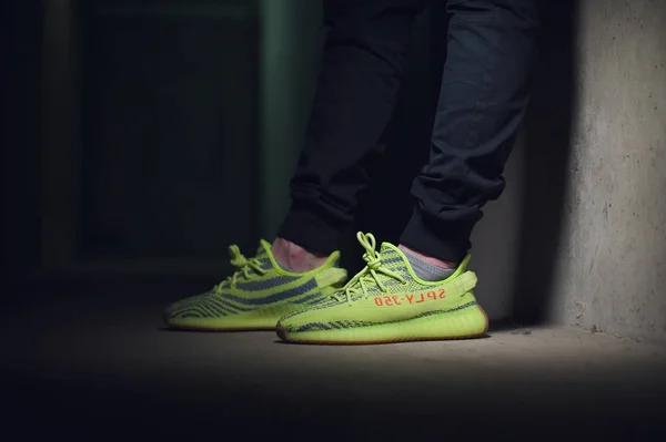 Ένας άντρας που φοράει Adidas Yeezy Boost 350 v2 Sply ημι-παγωμένα κίτρινα αθλητικά παπούτσια σε σκούρο γκρι φόντο. Γκρο πλαν άποψη των πάνινα παπούτσια. Krasnoyarsk, Ρωσία - 26 Δεκεμβρίου 2017 — Φωτογραφία Αρχείου