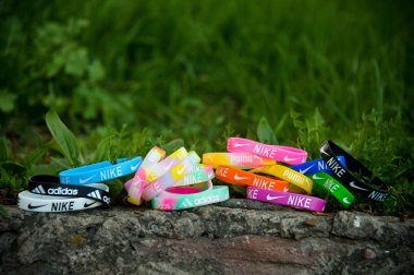 Renkli lastik bileklikler, Nike, Adidas, Puma markalarının etiketli bileklikler kayalarda ve yeşil çimen arka planda. Gökkuşağı rengi silikon bilezik..