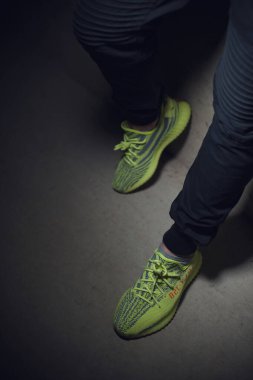 Adidas Yeezy Boost 350 v2 Sply yarı donmuş sarı spor ayakkabılı koyu gri arka planda bir adam. Spor ayakkabılara yakından bak. Krasnoyarsk, Rusya - 26 Aralık 2017