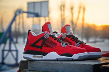 Fire Red Nike Air Jordan IV Retro basketball shoes in sunset light. Famous sneakers shot outdoors at the basketball court background. Krasnoyarsk, Russia - February 7, 2015 clipart