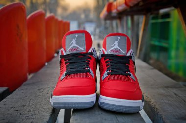 Front view of famous Nike Air Jordan IV Retro basketball shoes in fire red and black colors shot outdoors at wooden background. Sport footwear concept. Krasnoyarsk, Russia - February 7, 2015 clipart