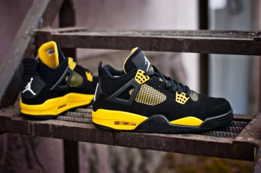 Black yellow Nike Air Jordan IV 4 Retro basketball shoes shot outdoors on rusty metal stairs background.. Detailed view of sneakers by famous brand. Krasnoyarsk, Russia - February 11, 2015 clipart