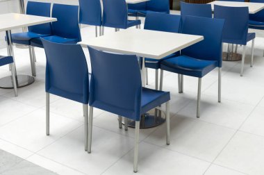 Mavi plastik sandalyeli ve beyaz masalı halka açık yemek alanının içi. Alışveriş merkezindeki yemek katında boş masa, modern iç tasarım..