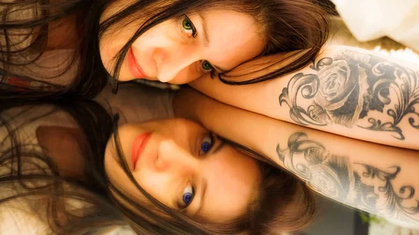 beautiful green-eyed brunette with a tattoo lies on the mirror and sees her reflection with blue eyes