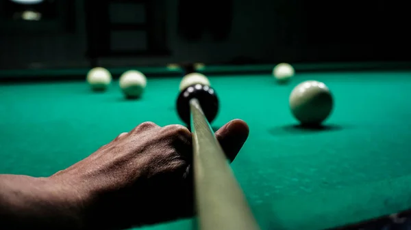 Bilardo oyuncusu bilardo ıstakasında kırmızı topa yeşil bir kumaşa vurmayı hedefliyor.