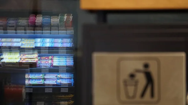 Photo of a trash can with a pictogram of a person throwing out trash on a background of blurry reflection of snacks and chewing gums