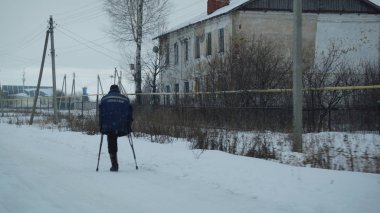 Tek bacaklı yalnız bir adam karlı bir köyde koltuk değnekleriyle yürüyor.