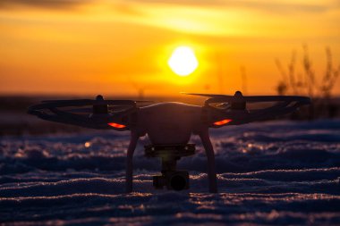 Batan güneşe karşı karda duran bir dronun fotoğrafı.