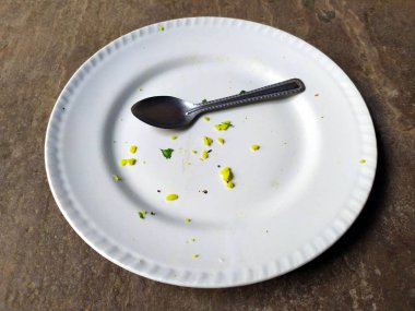 Beyaz kilden bir tabak, biraz yiyecek ve arka planda izole edilmiş bir kaşık.