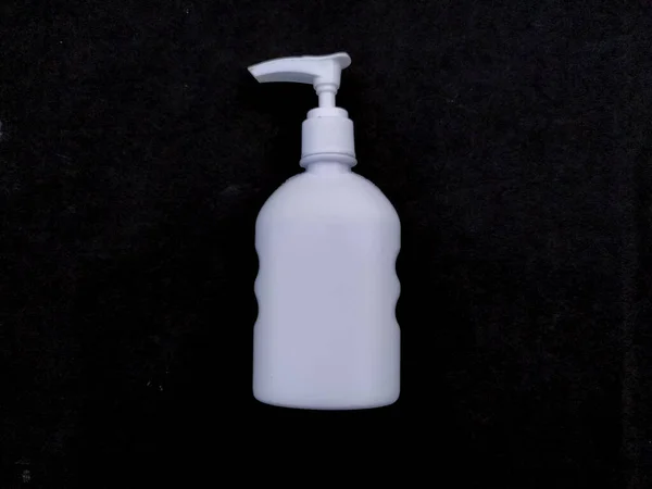 Beyaz plastik el dezenfektanı şişesi siyah arka planda izole edilmiş.