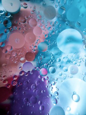 Renkli bir yüzeyde cam bir kâsede yağ ve su.