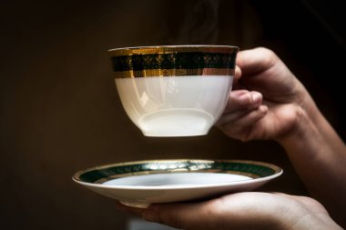 Eller bir fincan çay tabağı ve bir fincan sıcak kahve tutuyor.