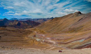 Vinicunca Vadisi 'ndeki Apu Ausangate ve Rainbow Mountain Peak' in arkasında. Yoğun kırmızı, sarı, turuncu, yeşil ve mavi renkleri olan And Dağları sıradağları. Tepedeki izleme noktasında ziyaretçiler var. 