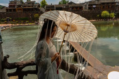 Beyaz şemsiyeli genç Çinli kadın gelinler için geleneksel yerel elbiselerle poz veriyor. Fenghuang Antik Kenti, Hunan Bölgesi, Çin