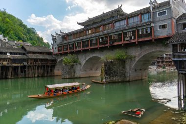 Günlük hayatın mükemmel bir resmi. Eski Hongqiao taş köprüsünü geçmek üzere olan küçük bir balıkçı teknesi. Fenghuang Antik Kenti, Hunan Bölgesi, Çin  