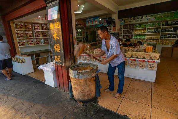 Dükkandaki yaşlı adam, Çin 'in Hunan bölgesindeki Fenghuang Antik Kasabası' nda yerel bir tatlıyı hazırlayan tahta bir topuz tutuyor.