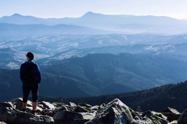 Genç bir adam ya da bir adam bir kaya dağının tepesinde duruyor ve inanılmaz bir dağ manzarasının tadını çıkarıyor. Turist, gezgin, sporcu. Ukraynalı Karpatlar. Yürüyüş, spor, tırmanış, seyahat