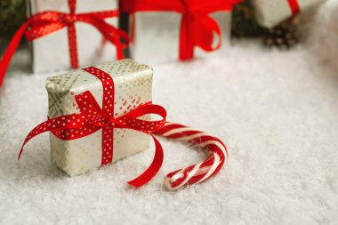 Parlak kırmızı kurdele ve fiyonklu paket, çizgili Noel bastonu ve beyaz kabarık bir yüzey üzerindeki diğer süslemeler. Arkadaşlar, aileler ve sevgililer için kış tatili hediyeleri. Kapatın.