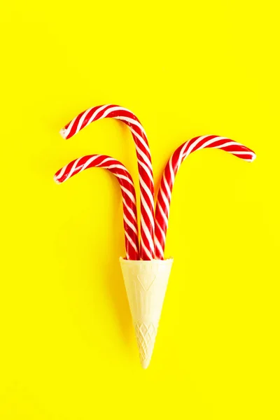 Creative Christmas still life with food, top view. Three Christmas canes in a waffle cone for ice cream on a bright yellow background, close up. Winter holidays concept.