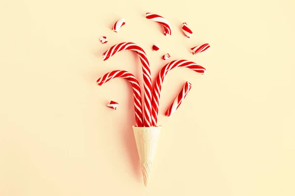 Creative Christmas still life with sweets, top view. Three Christmas canes and pieces of candy in a waffle cone for ice cream on a pastel pink background, close up. Winter holidays concept, minimalism.