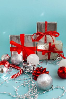 Gümüş, kırmızı ve mavi renkli Noel tebrik kartı tasarımı. Paketlenmiş hediyeler, parlak Noel topları, fiyonklar, gümüş boncuklar ve açık mavi arka planda parlak bir şeker kamışı.