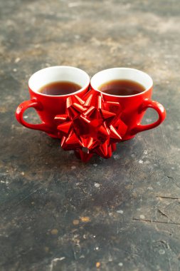 İki parlak kırmızı kahve fincanı ya da koyu desenli beton bir masada dekoratif fiyonk. Sevgililer Günü romantik randevu konsepti, yakın çekim.