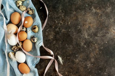 Güzel Paskalya yumurtaları. Doğal renklerde organik tavuk ve bıldırcın yumurtalarının karışımı mavi keten havluyla tüylü, pastel pembe kurdeleli ve küçük beyaz çiçeklerle dolu bir hayat. Basit Paskalya kartı tasarımı, metin için kopyalama alanı