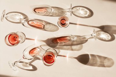 Gül şarabı ya da şampanyalı bardaklar beyaz masanın üstünde duruyor. Güzel, yaratıcı natürmort hayat, sert gölgelerle ve camdan parlayan ışıkla doludur. Parti konsepti, seçici odak