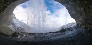 Tourists looking at view through cave at waterfall clipart