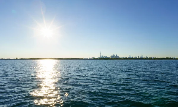 Skyline de la ciudad distante con la luz del sol en la superficie del agua — Foto de Stock