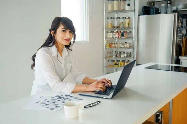 Mujer joven usando el ordenador portátil en la cocina en casa. — Foto de Stock