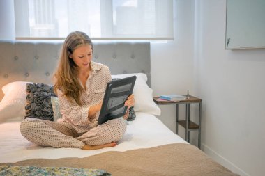 Genç kadın yatakta dijital tablet kullanarak pijama