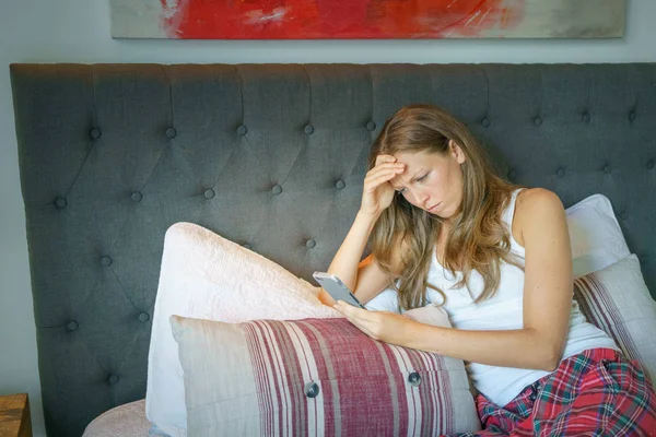 若い女性のテキスト メッセージング スマート フォンのベッドの上に横たわっている間心配してください — ストック写真