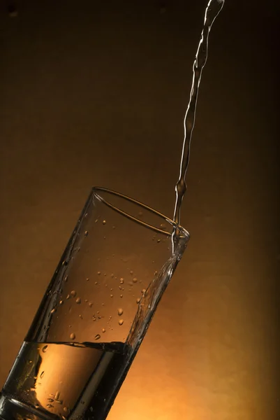 glass of water with water splash on orange background