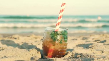 Misted glass of drink on sand on beach