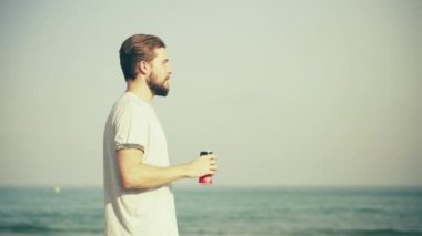 Genç adam sahilde içki içiyor.