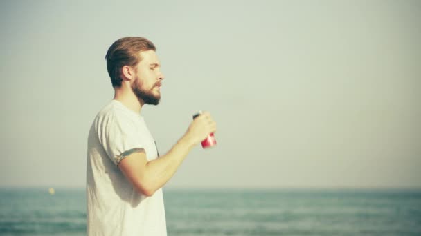 Young Man Drinking Beverage on Beach — Stock Video