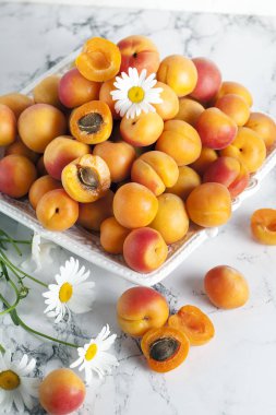 ripe apricots with daisies on a white plate on a light backgroun