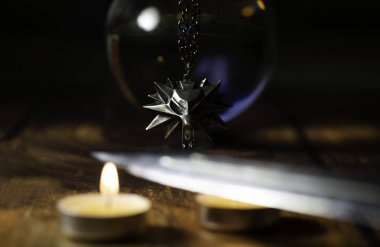 Nizhyn, Ukrayna / 22 Aralık 2019: Cadı Geralt 'ın madalyonu mum ışığının üzerinde kristal top ve bıçağın arkasında asılı duruyor. Yeni Netflix TV dizisi prömiyeri 
