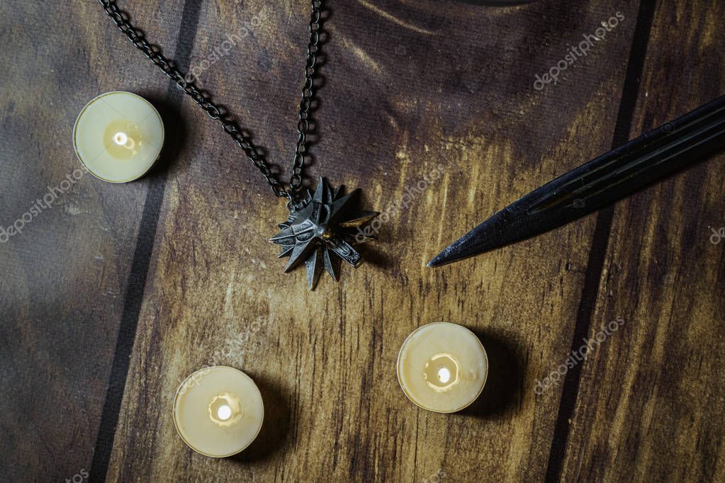 Nizhyn, Ukraine/ 22 December 2019: Flatlay, closeup of witcher Geralt's medallion, knife and candles on the wooden background. New Netflix TV-series 