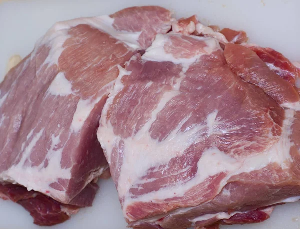 A man cuts fresh meat pork on a white Board