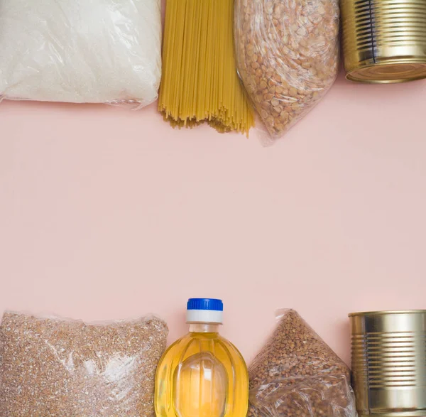 Food stocks crisis food stocks for the period of quarantine isolation on a pink background. Spaghetti macaroni, canned food, butter, sugar, buckwheat. Food delivery, donation, coronavirus quarantine.