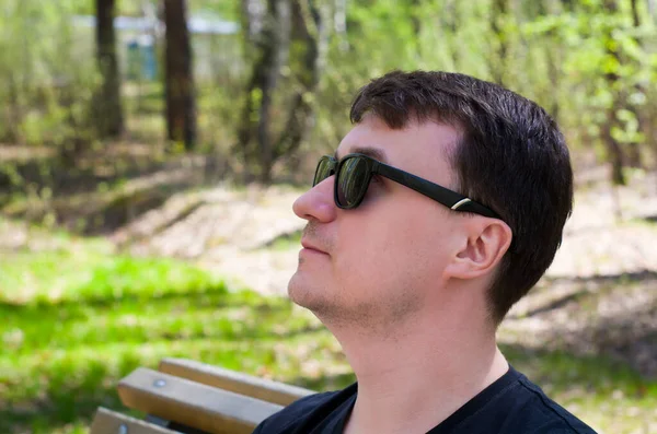 Close-up of a happy calm young European thoughtful guy, in dark glasses, looking up, visualizing the future, planning a weekend leisure, relaxing in the Park